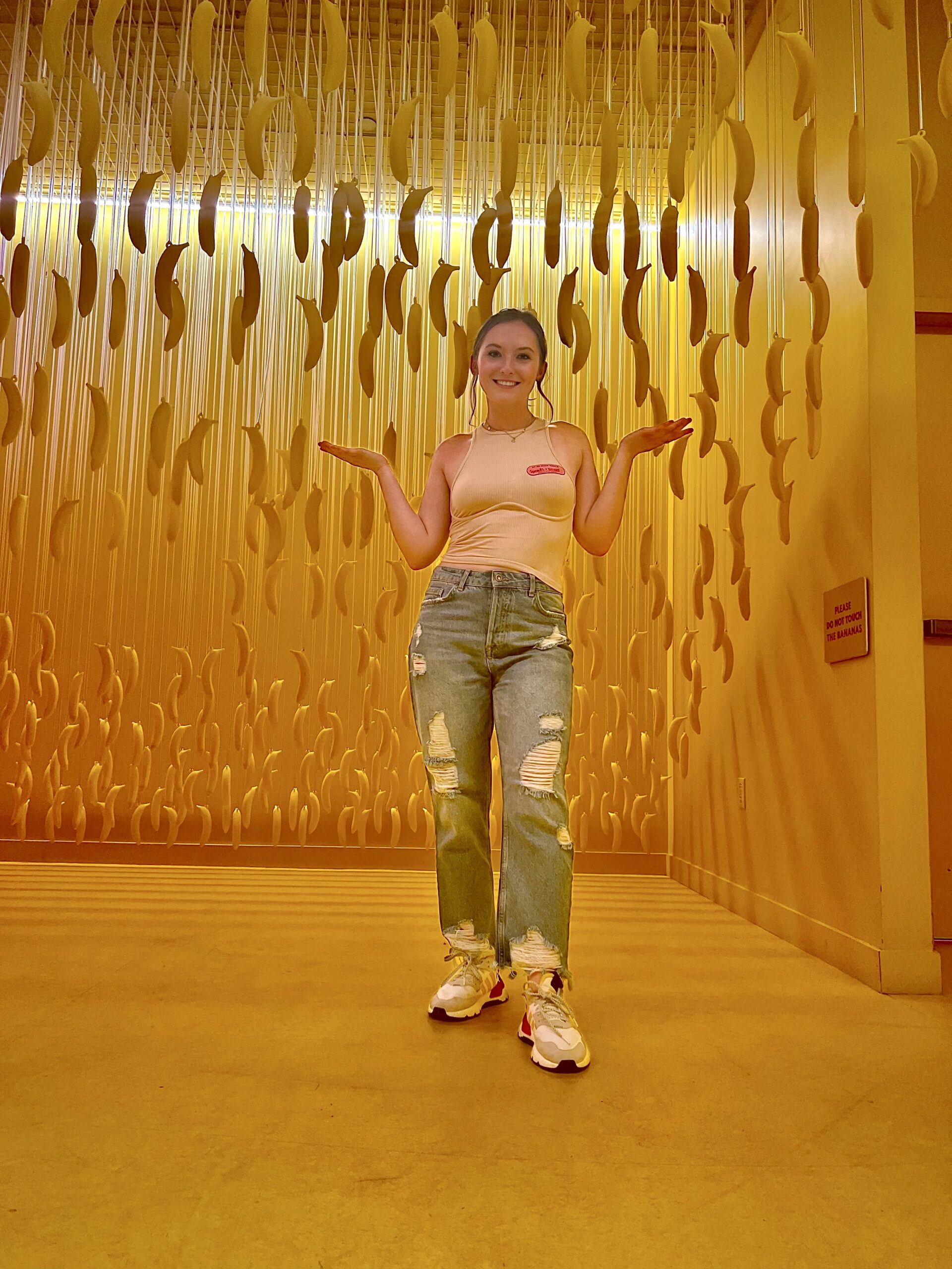 picture of Kayla in a room of bananas hanging from the ceiling