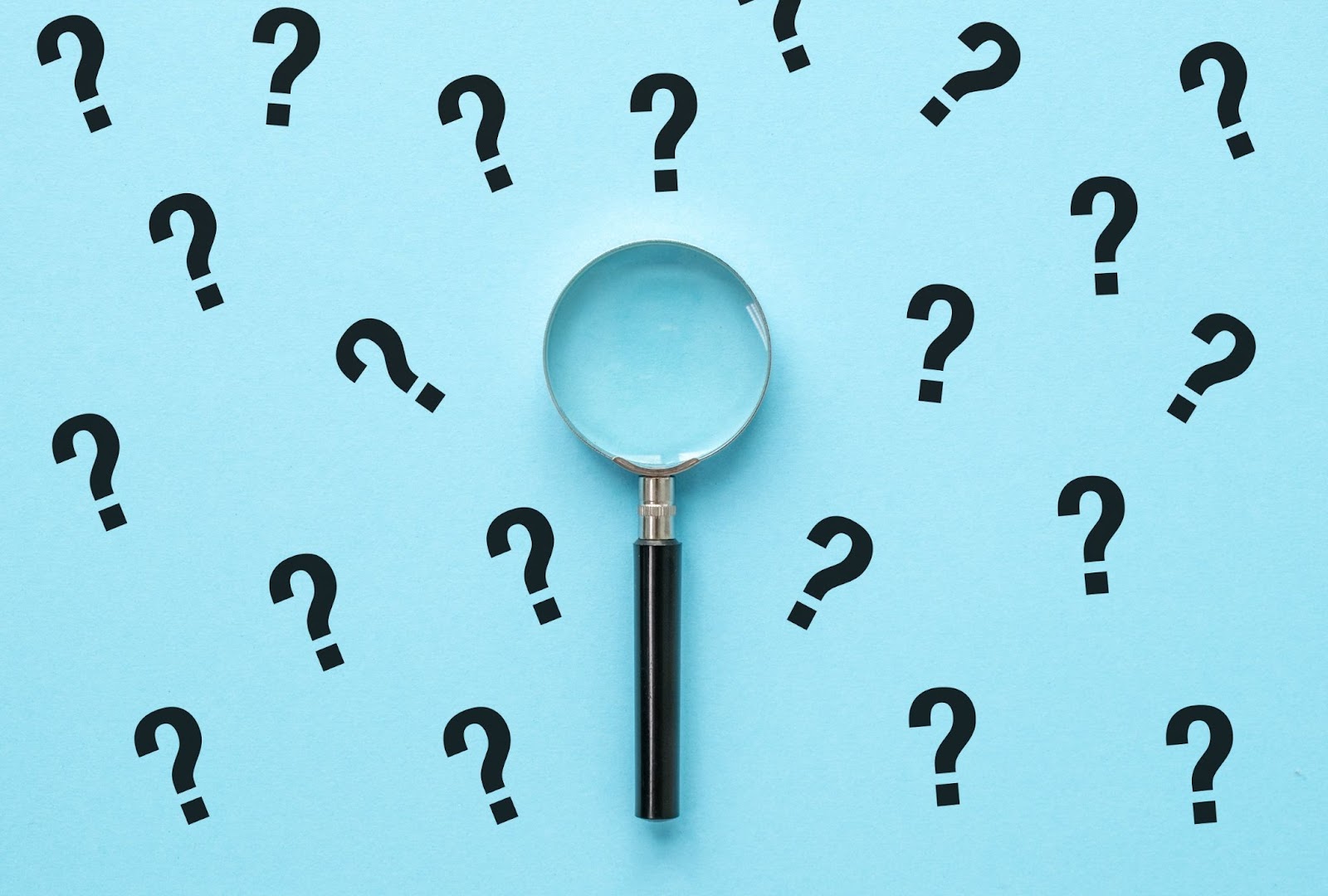 Magnifying glass placed on a blue background surrounded by scattered black question marks.