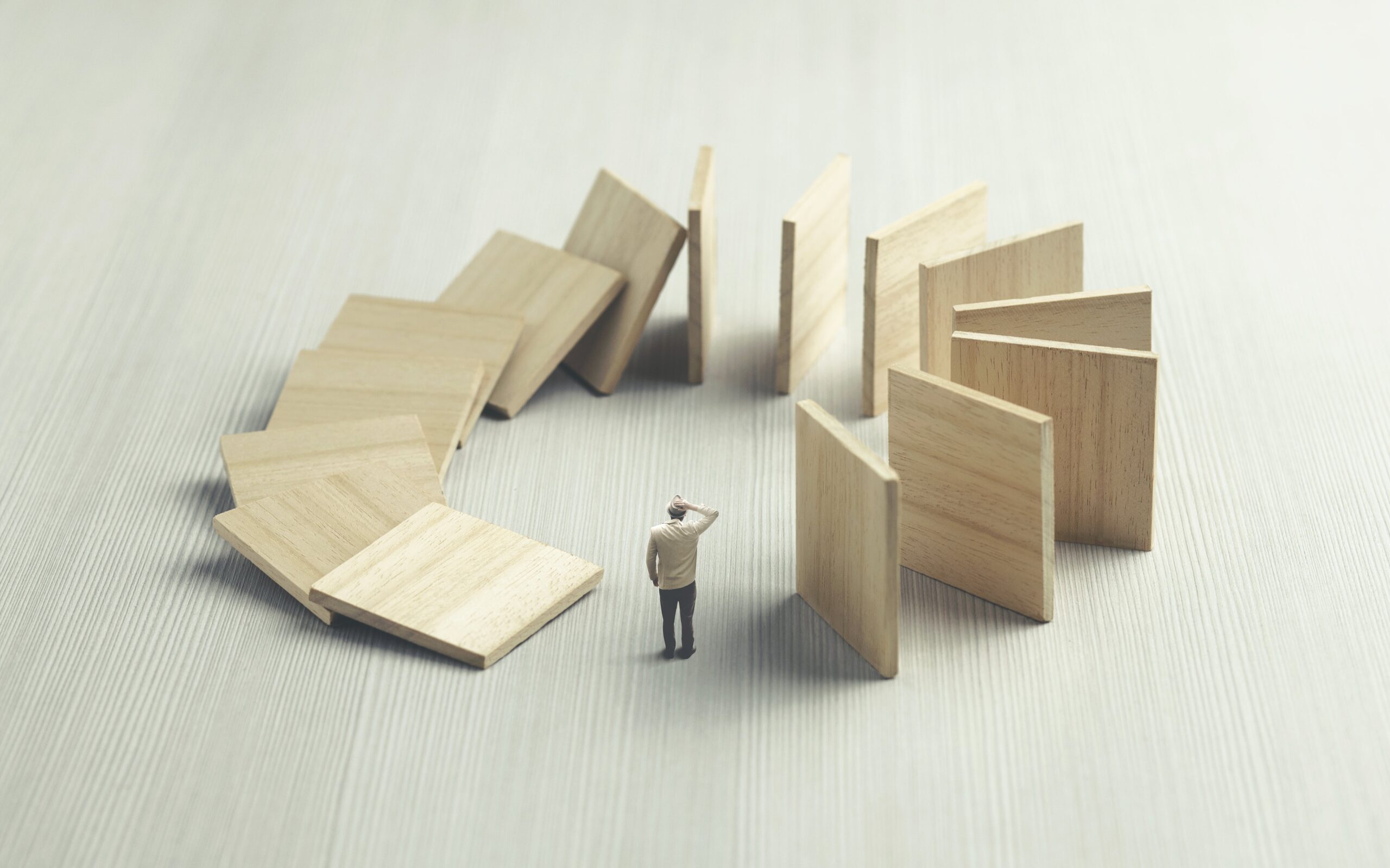 Confused man watching wooden dominos collapsing on him, surreal concept.