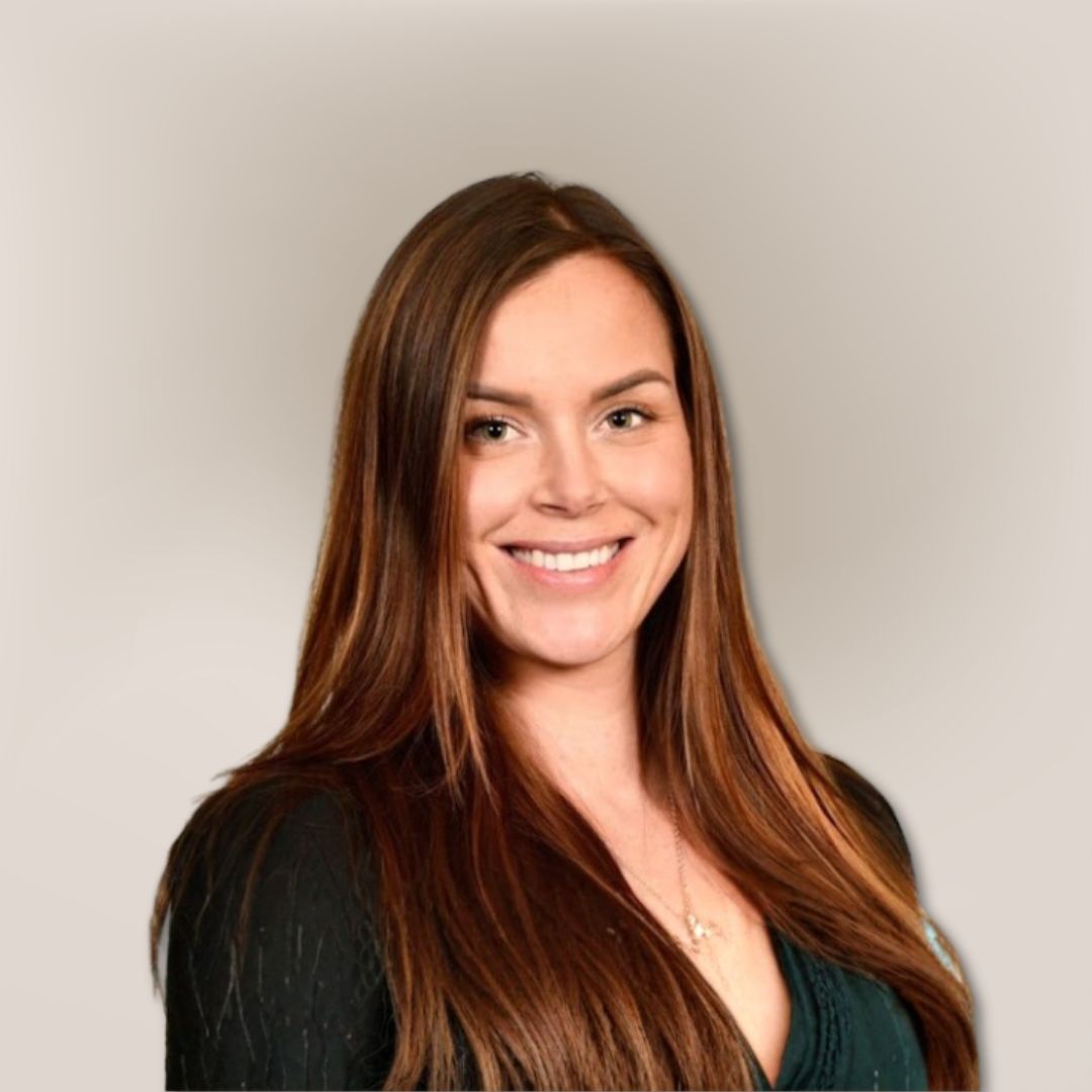 Smiling woman with long, straight brown hair, wearing a dark top and a necklace, posed in front of a plain, light-colored background—Samantha Behiry.