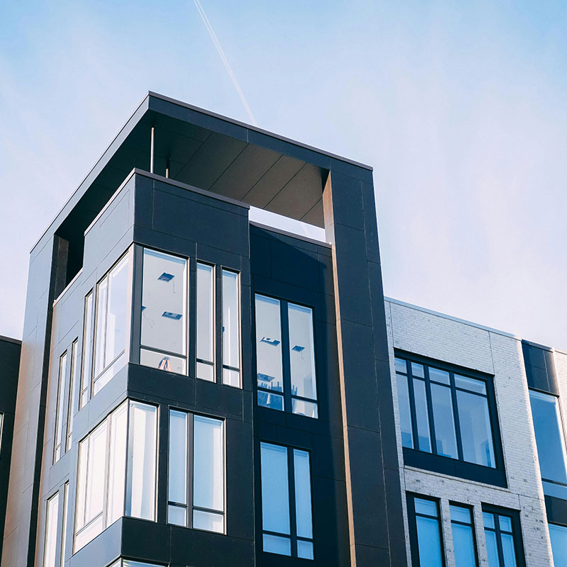 Modern apartment building with large glass windows and a dark exterior facade, set against a clear blue sky