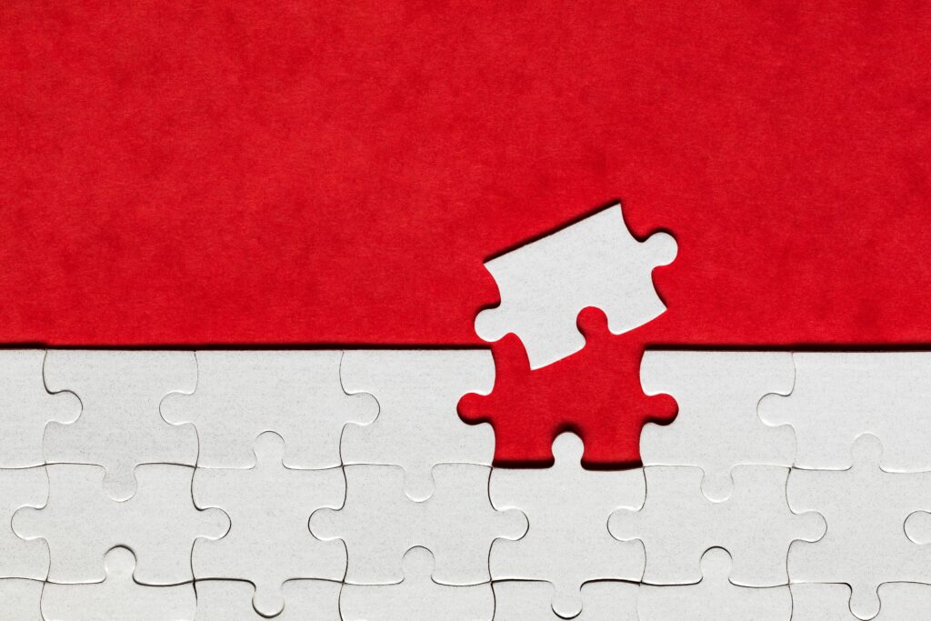 A nearly completed white jigsaw puzzle with one missing piece being placed into the empty spot, set against a red background—symbolizing how search is moving from traffic to trust, perfectly fitting the final piece for meaningful connections.