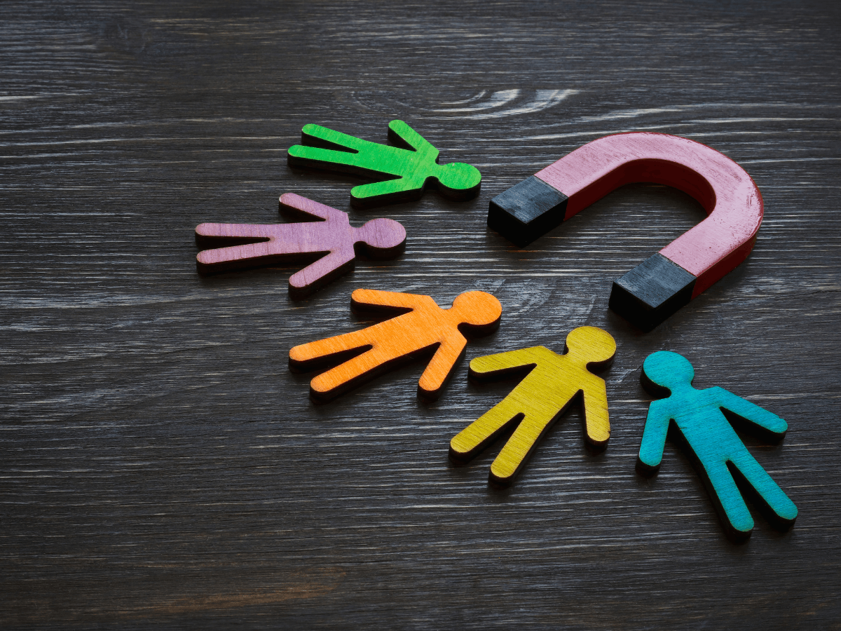 A red horseshoe magnet attracts five colorful human-shaped figures on a dark wooden surface, symbolizing attracting people or social engagement—a vivid representation of resident retention and growth strategy.