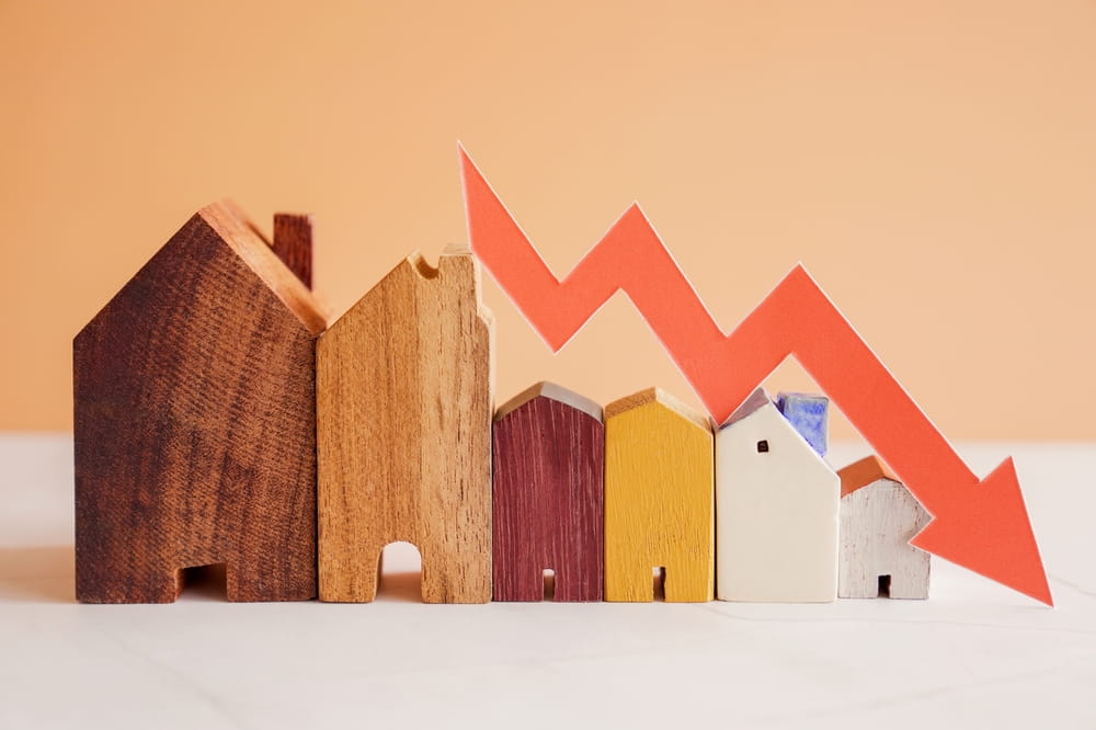 Several wooden house models of varying sizes are lined up, with a red downward arrow above them, symbolizing a decline, possibly in rent growth or property values—a trend that multifamily operators may be closely monitoring.
