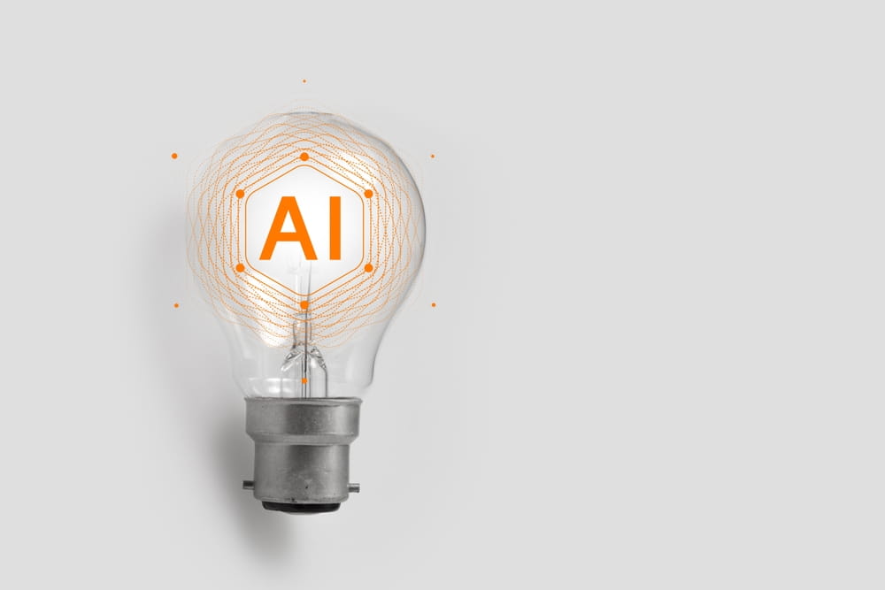 A lightbulb with the letters AI glowing inside, surrounded by orange lines, symbolizing Marketing AI and innovation on a plain gray background.